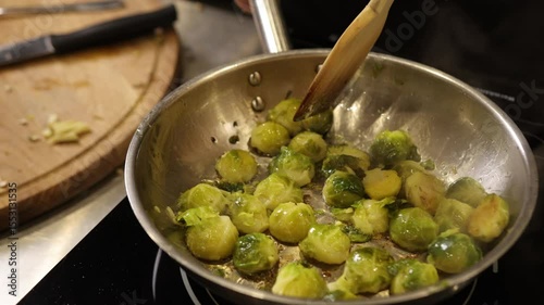 Active cooking, saute pan, vegetable cooking. In kitchen, hand stirs sauteing Brussels sprouts in stainless steel pan, highlighting healthy cooking process using fresh produce.