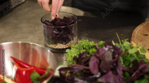 Basil pesto, rustic cooking, pesto sauce. Carefully placing fresh herbs, basil, and pine nuts into food processor, hands are ready to make pesto in setting that highlights natural cooking