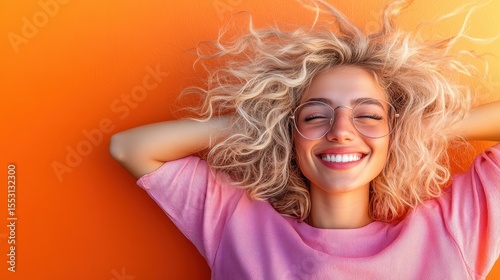 This vibrant image showcases a joyful young woman with curly hair and glasses, exuding happiness against a bold orange background, embodying a carefree spirit.