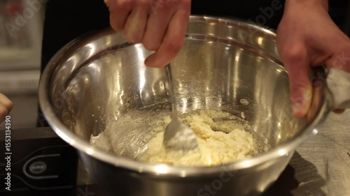Stirring ingredients, mixing bowl, metal bowl. Close-up person stirring ingredients in large metal mixing bowl, using spoon. Person's hands are visible, holding bowl steady while preparing recipe