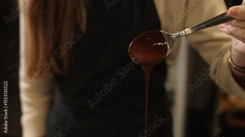 Chocolate flow, smooth chocolate, close-up. In focused close-up, melted chocolate streams smoothly off spoon into sleek stainless steel bowl, emphasizing meticulous preparation involved in desserts.