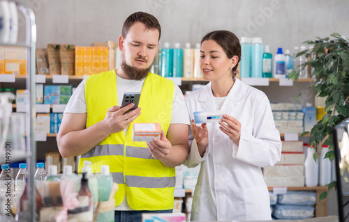 Laborer man builder in pharmacy scans QR code on antiallergic pills, studies item in detail, collects information online, uses quick link to access drugs instructions. Girl pharmacist offer help for photo