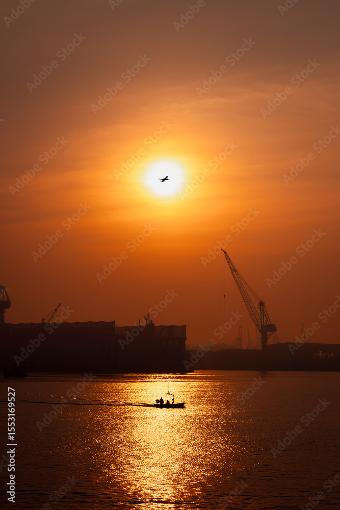 Obraz premium morning scene golden hour of the sun is rising, silhouette of shipyard working or mantainance and repair by crane, silhouette of plane and fishing boat full speed