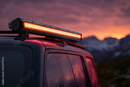 Close-up of a dark vehicle roof with an illuminated orange LED light bar mounted on top against a colorful sunset sky with mountains in the background