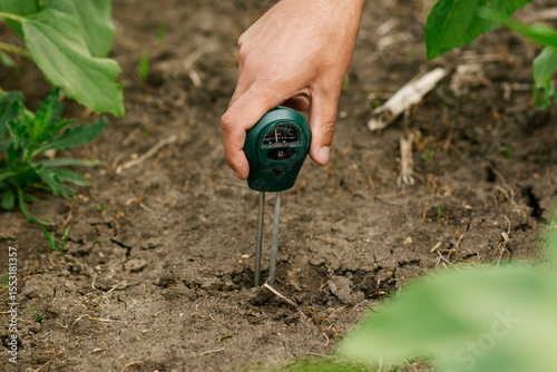 Close-up of a male hand holding a soil moisture meter inserted into the ground. Soil moisture measurement, precision agriculture, sustainable farming practices. 
