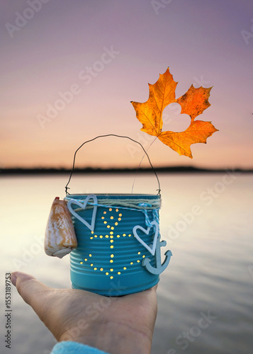 hand is holding an anchor Lantern with Candle and Autumn Leaf by the Sea