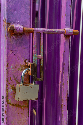A metallic padlock secures a rusted latch on a weathered purple gate
