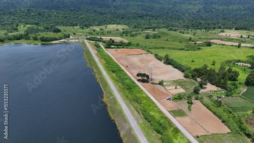 Drone footage of aerial view of Lam Phra Phloeng reservoir and surrounding farmland in Wang Nam Khiao, Nakhon ratchasima, Thailand. Scenic landscape of countryside with curved rural roads