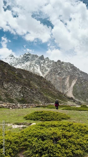4K Vertical video of teenager backpacker girl hiking in mountains during summer season. Green meadows and cloudy sky in Himalayas at Miyar Valley, Himachal Pradesh, India. Girl enjoying summer holiday