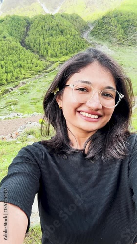 4K Vertical selfie shot of Indian girl enjoying summer holidays in mountains in Sural Bhatori, Himachal Pradesh, India. Travel, tourism and hiking outdoors concept. Girl having fun while trekking. 