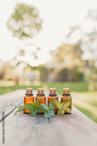 Collection of four amber essential oil bottles in natural outdoor setting with fresh herbs