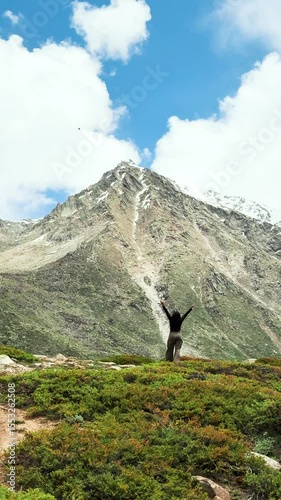 4K Vertical shot of teenager girl tourist raising hands while hiking in mountain at Miyar Valley, Himachal Pradesh, India. Indian girl enjoying nature and doing outdoor adventure activities. 