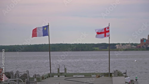 Acadian and Mi'kmaq flags waving along waterfront dock in tranquil scene