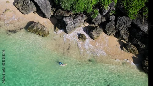 Aerial view of adult man with surfboard walking at beach near the beautiful cliff.Bali.Indonesia