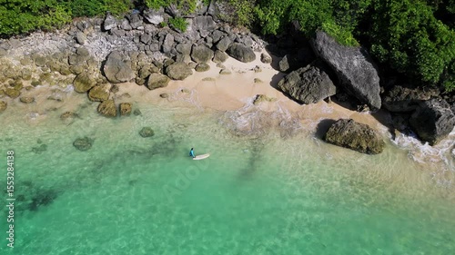 Aerial view of adult man with surfboard walking at beach near the beautiful cliff.Bali.Indonesia