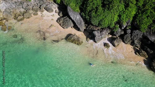 Aerial view of adult man with surfboard walking at beach near the beautiful cliff.Bali.Indonesia