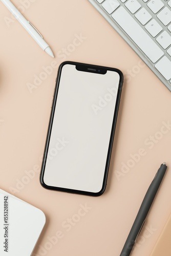 Modern smartphone on desk with keyboard, pens, and notebook