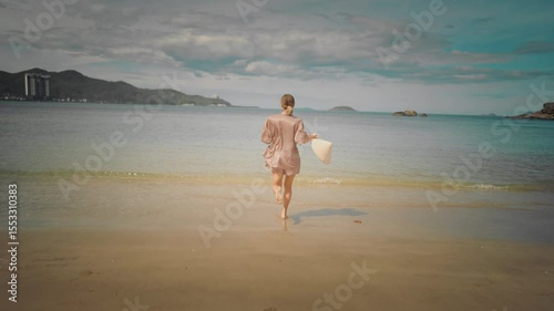 Carefree woman running to ocean, slow motion back view, follow shot on beach. Happiness and joy in summertime, beautiful sandy seacoast and graceful lady, summer trip to sea, amazing cloudscape