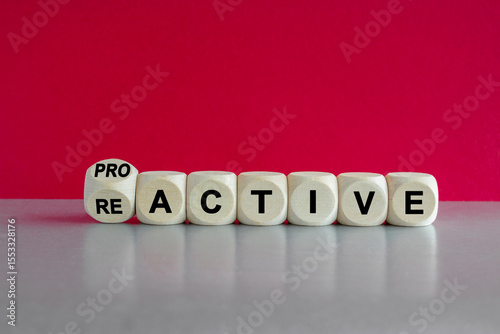 Turned a dice and change the word reactive to proactive. Beautiful pink background, grey table. Business and reactive or proactive concept