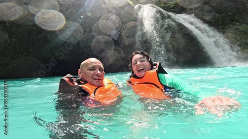 Couple floating and smiling under waterfalls during canyoneering in Kawasan Smiling couple enjoying waterfall canyoneering in Kawasan, Philippines