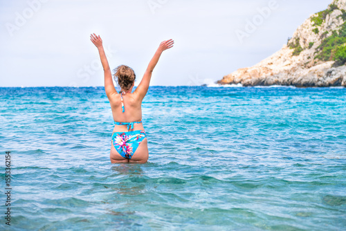 Woman tourist swimming bathing in turquoise Mediterranean water of Iero beach on Ikaria island Greece cove near Faros, Ikaria with Ikarian sea cliff