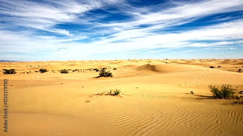 Expansive desert landscape under a blue sky with wispy clouds and gentle dunes in the background