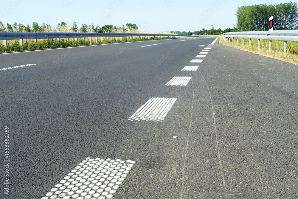 Obraz premium Highway infrastructure and traffic control innovations in Serbia: modern asphalt road with raised pavement markings made of white painted dots, highlighting road safety technology, tactile guidance