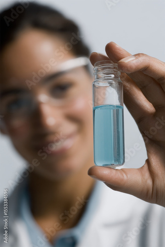 lab technician with cheerful expression positioned on right side of frame intently examining test tube filled with