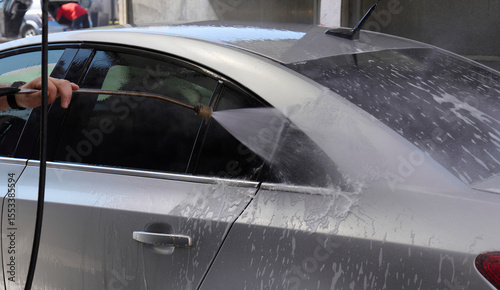 Water is sprayed on a silver sedan during a car wash activity outside