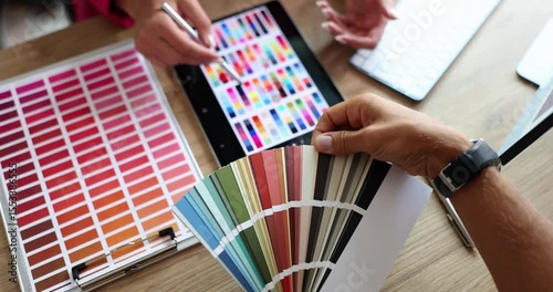 Designers discuss color palettes for project using digital tablet and color swatch. Professionals show collaborative process and color selection