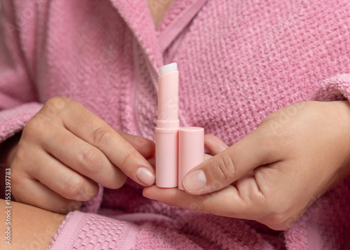 Woman in pink bathrobe holding in hand opened lip balm stick with a lid closeup, girly mockup