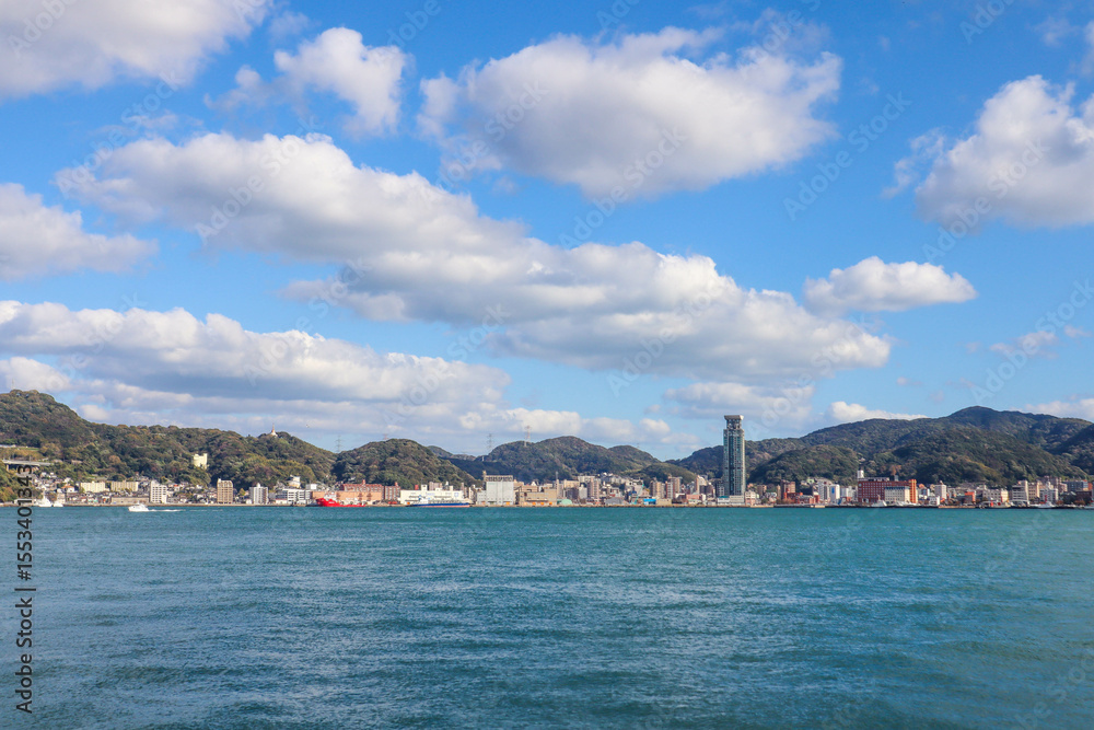 Fototapeta premium Panoramic View of Kitakyushu Skyline with Mountains and Ocean under Blue Sky, Japan