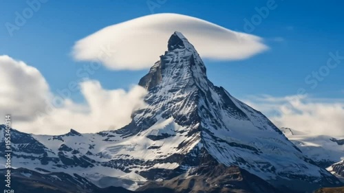 Sharp snow-covered peak with lenticular cloud above under blue sky, seamless looping 4k time-lapse animation video background. Nature concept