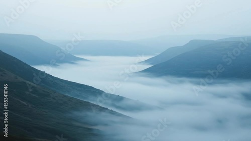 Fog drifting through deep mountain valleys in cold dawn with blue tones, seamless looping 4k time-lapse animation video background. Nature concept