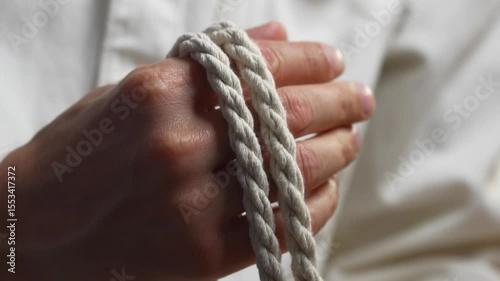 A man in a white shirt winds a long and strong rope around his hand.
A white rope in a man's hands to tie something