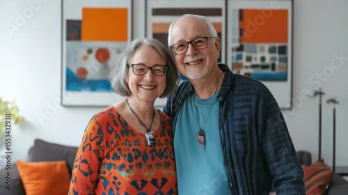 Smiling elderly couple wearing glasses cozy living room with colorful abstract painting and cushions, happy indoors with medical alert pendants