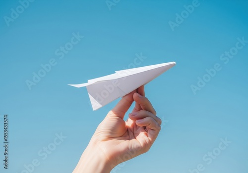 A hand launches a white paper airplane against a clear blue sky, symbolizing freedom and dreams.
