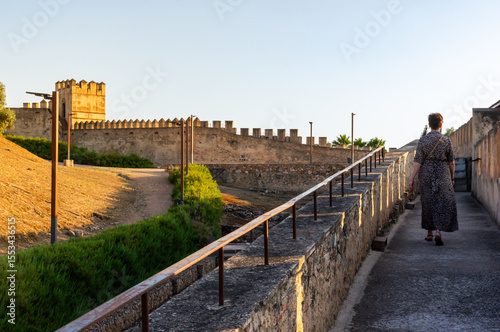Solitude and Stone: A Woman Walks Along the Alcazaba Walls at Sunset.