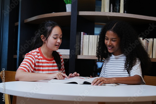 Two teenage girls happily chatting together about their homework and reading books in the school library.