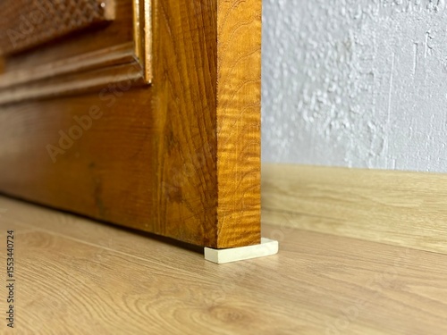 Improvised door stopper using a white rubber eraser under an old wooden door on a laminate floor