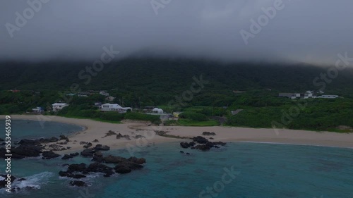 Aerial view of coastal houses by sandy beach and blue water on foggy morning