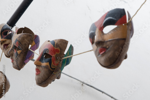 Traditional carnival masks hanging on clothesline against white sky. Colorful papier-mâché faces with expressive features showcase European folk art.
