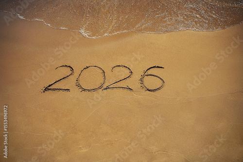 Hand-drawn numbers 2026 of new year on wet yellow sand on beach,
