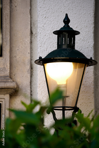 Wall mounted lantern. Glowing vintage bulb. Iron street fixture. Textured white wall.

