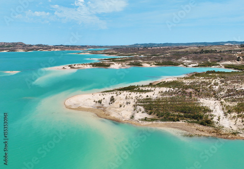 Aerial view of Embalse de La Pedrera reservoir landscape, with striking turquoise waters, curving white-sand shores, and desert-like hills in distance. Costa Blanca. Province of Alicante. Spain