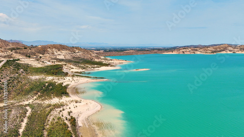 Aerial view of Embalse de La Pedrera reservoir landscape, with striking turquoise waters, curving white-sand shores, and desert-like hills in distance. Costa Blanca. Province of Alicante. Spain