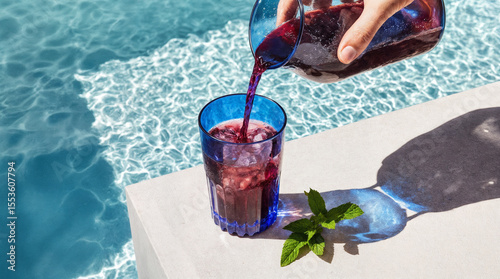 Refreshing sangria being poured into blue glass beside swimming pool  