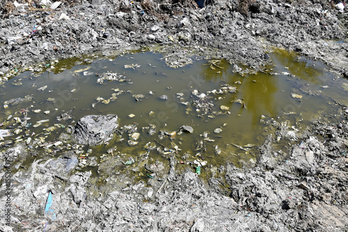 polluted stagnant water puddle in garbage dump area under sunlight, urban environmental pollution
