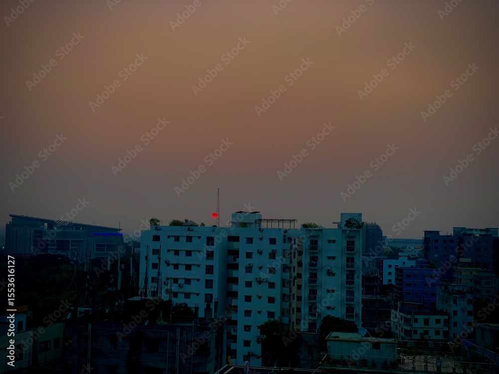Fototapeta premium Cityscape at dusk with a red sun and buildings