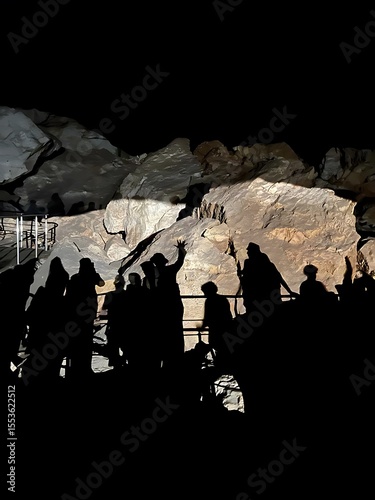 Fotografie Group of people exploring a cave with lit rock formations in background